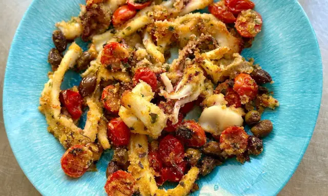 Calamari gratinati al forno su piatto blu, con pomodorini e olive. Croccanti e saporiti, un piatto che profuma di mare.