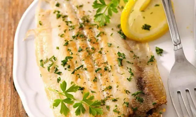 Sogliola al forno, dorata e profumata, guarnita con prezzemolo fresco e spicchi di limone. Un piatto leggero e saporito.