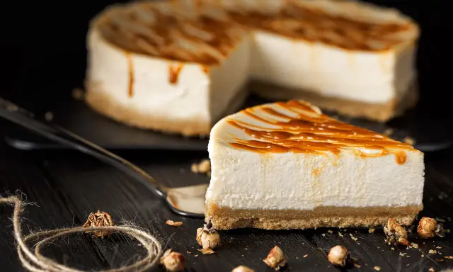Una fetta di cheesecake senza gelatina, con colatura di caramello, su un piatto scuro.