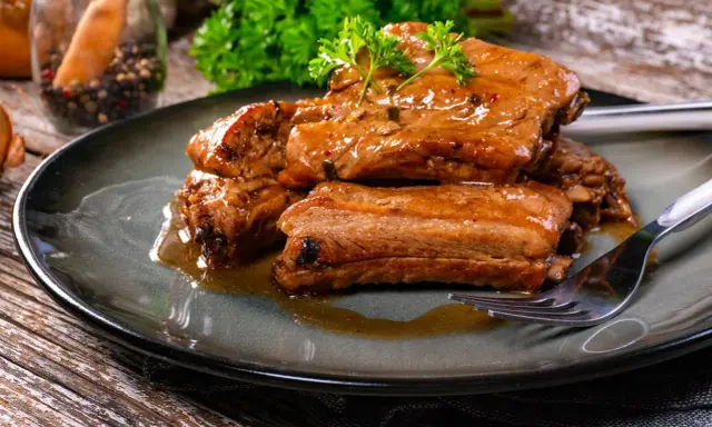 Succulente costine di maiale glassate, guarnite con prezzemolo fresco, servite su un piatto scuro con una forchetta.