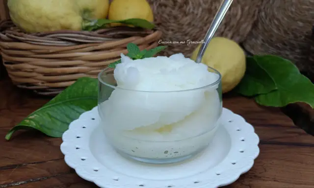 Granita al limone fatta in casa, fresca e dissetante, servita in una coppetta con foglioline di menta. Limoni freschi in un cesto sullo sfondo.