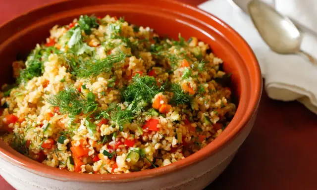 Tabulè di verdure fresco e colorato, con pomodori, zucchine e erbe aromatiche, servito in una ciotola di terracotta.