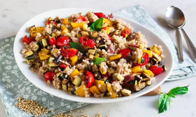 Un piatto colorato di insalata di grano saraceno con verdure miste arrosto: peperoni, zucchine, melanzane e pomodorini.