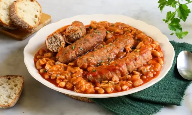 Piatto di salsiccia e fagioli in umido, servito con pane tostato.
