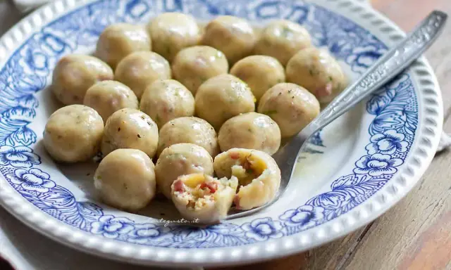 Gnocchi di pane su piatto decorato, uno spezzato rivela un ripieno saporito.