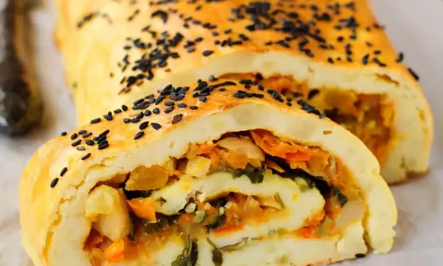 Rotolo di patate dorato, cosparso di semi neri, con un ripieno colorato di verdure.