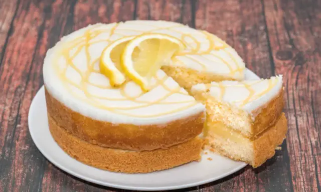 Torta al limone soffice e profumata, con glassa bianca e decorazioni gialle, guarnita con fette di limone.