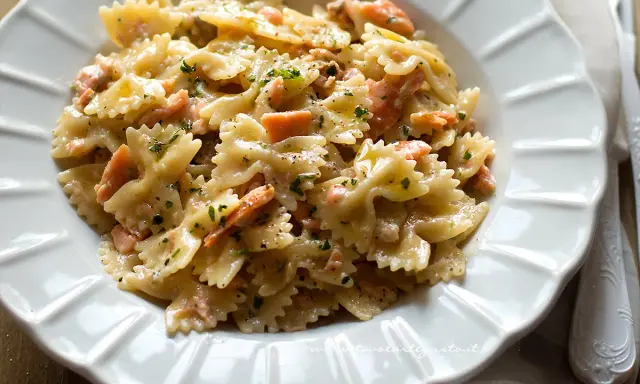 Farfalle cremose con salmone affumicato, un piatto gustoso e invitante, guarnito con prezzemolo fresco e pepe nero.