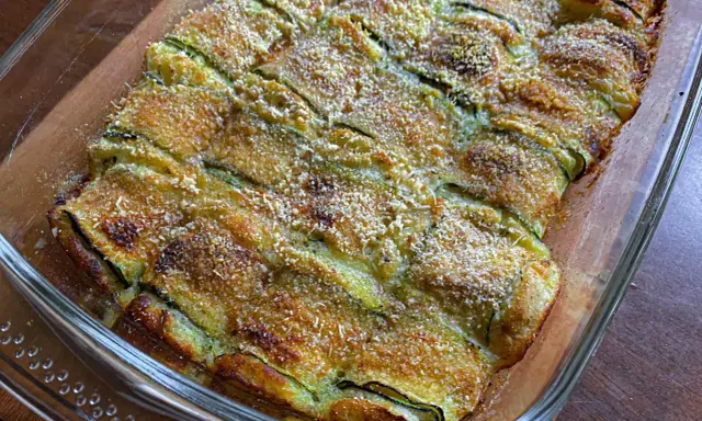 Involtini di zucchine grigliate al forno, dorati e croccanti, in una pirofila di vetro.