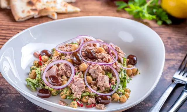 Insalata di ceci e tonno con olive nere e cipolla rossa, servita in un piatto bianco su un tavolo di legno.