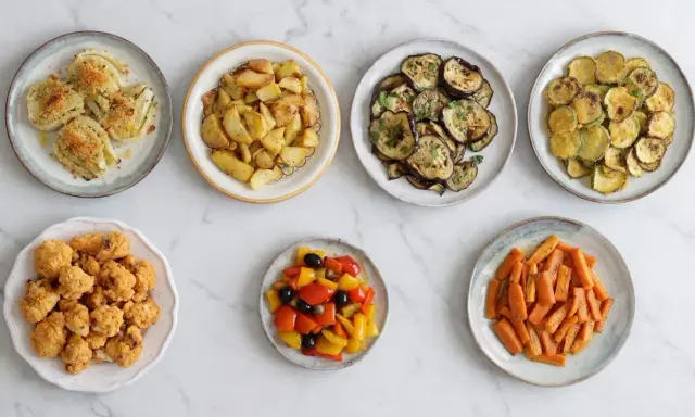 Sette piatti di verdure in friggitrice ad aria: finocchi, patate, melanzane, zucchine, cavolfiore, peperoni e carote.
