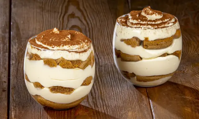 Due bicchieri di delizioso tiramisù senza uova, con strati di crema e savoiardi, spolverati di cacao.