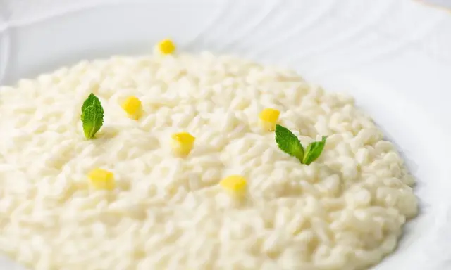 Un cremoso risotto al limone, guarnito con cubetti di limone e foglie di menta fresca, su un piatto bianco.