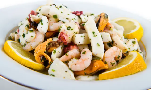 Deliziosa insalata di mare con verdure, gamberi, calamari, polpo e cozze, guarnita con spicchi di limone fresco e prezzemolo tritato.