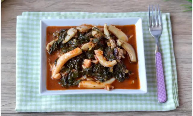 Un saporito piatto di seppie in zimino, con verdure scure e salsa rossa, servito su un tovagliolo a quadretti verdi.