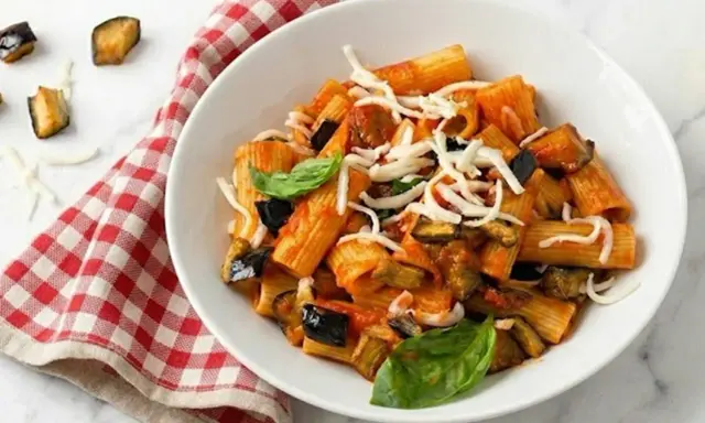 Piatto di pasta alla norma con melanzane fritte, pomodoro, basilico e ricotta salata grattugiata.