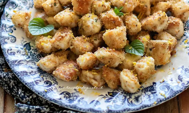 Bocconcini di pollo dorati e croccanti, guarniti con scorza di limone e foglioline di menta, serviti su un piatto decorato.