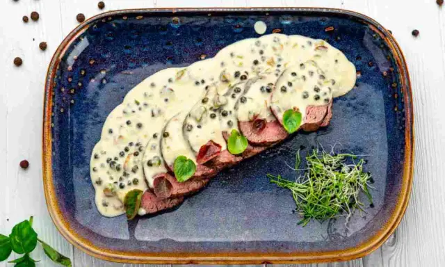 Fette affettate in salsa cremosa al pepe verde, guarnite con germogli freschi. Un delizioso filetto al pepe verde pronto da gustare.