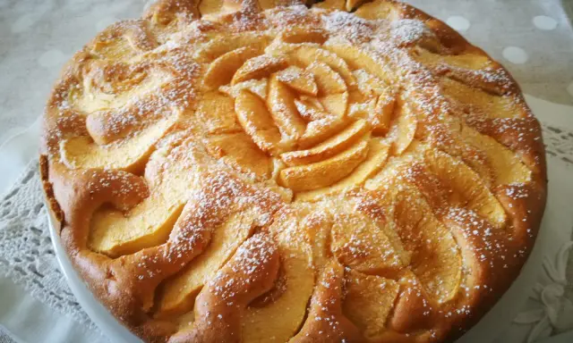 Deliziosa torta di mele senza glutine, decorata con fettine di mela disposte a rosa al centro e petali tutt'intorno, spolverata di zucchero a velo.