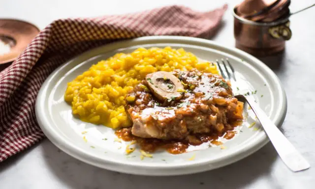 Un succulento ossobuco alla milanese, con il suo midollo invitante, adagiato su un letto di risotto giallo zafferano.