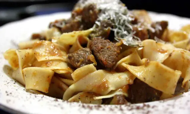 Pappardelle al cinghiale, un piatto ricco e saporito con pasta fresca e ragù di cinghiale, spolverato di parmigiano.