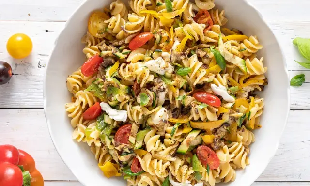 Un piatto invitante di pasta fredda saporita con fusilli, pomodorini, zucchine, peperoni gialli e mozzarella.
