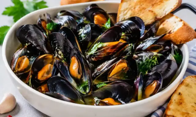 Soute di cozze fumante in una ciotola bianca, guarnita con prezzemolo fresco e accompagnata da fette di pane tostato.