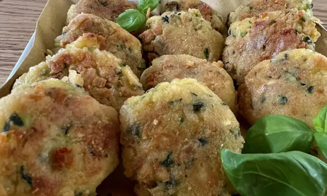 Deliziose polpette di zucchine grattugiate in padella, dorate e croccanti, guarnite con foglie di basilico fresco.