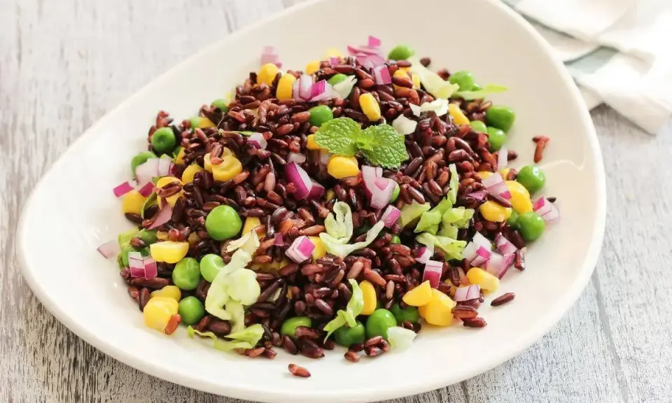 Insalata di riso Venere colorata con piselli, mais, cipolla rossa e lattuga croccante, guarnita con menta fresca.