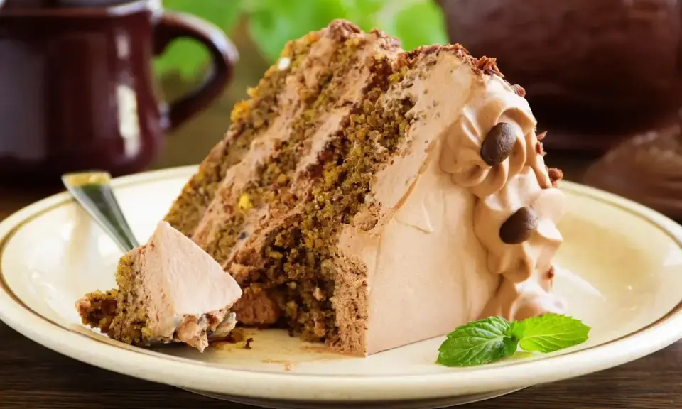 Una fetta di torta al cioccolato con abbondante crema al latte, guarnita con chicchi di caffè e una fogliolina di menta.