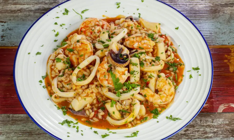 Un invitante risotto alla pescatora, ricco di gamberi, calamari e cozze, guarnito con prezzemolo fresco.