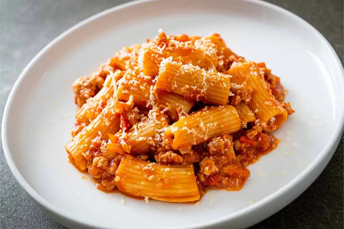 Piatto di pasta alla zozzona ricetta, con rigatoni conditi con rag&ugrave; ricco e abbondante parmigiano grattugiato.