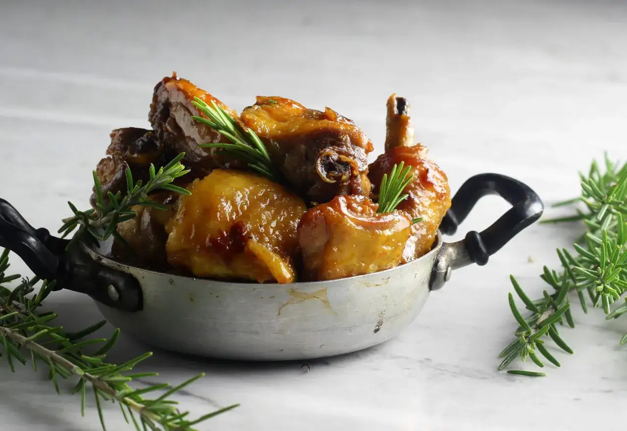 Succulento pollo alla birra, cotto in una piccola padella di metallo, guarnito con rametti di rosmarino fresco.