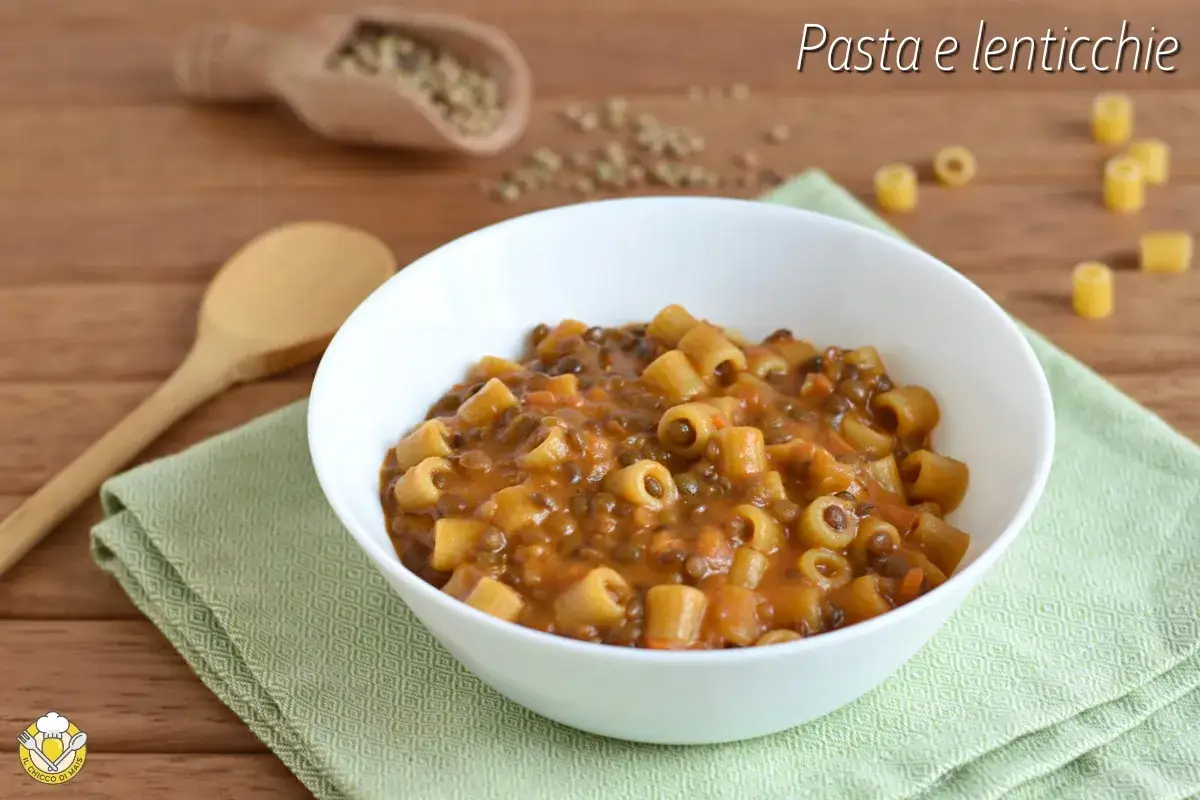 Un piatto fumante di pasta e lenticchie, servito in una ciotola bianca su un tovagliolo verde.