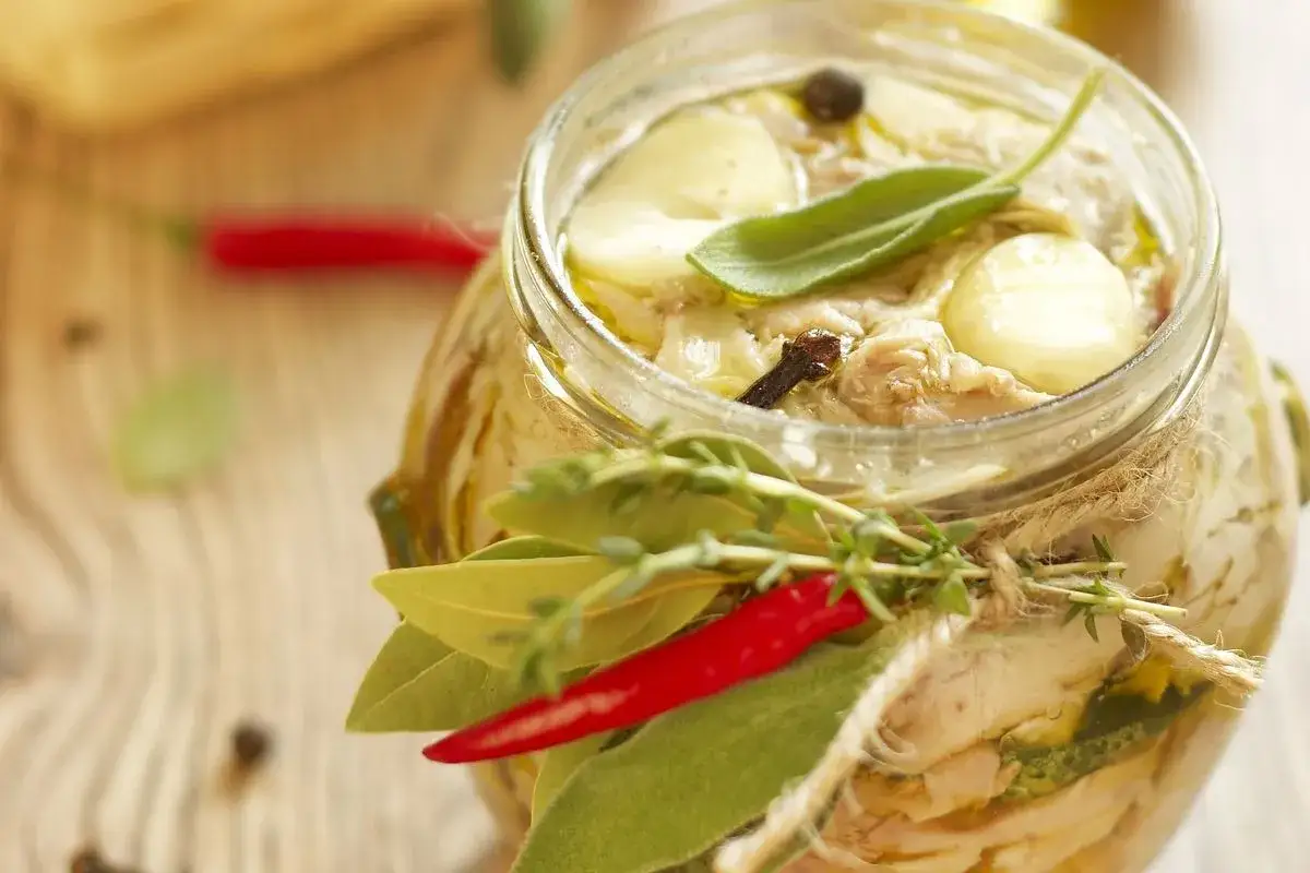 Vasetto di tonno di coniglio sott'olio, guarnito con erbe aromatiche, peperoncino e spezie.