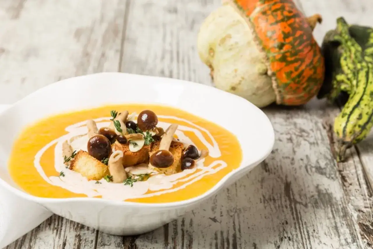 Vellutata di zucca cremosa, guarnita con funghi, crostini e erbe aromatiche, su un tavolo di legno rustico.