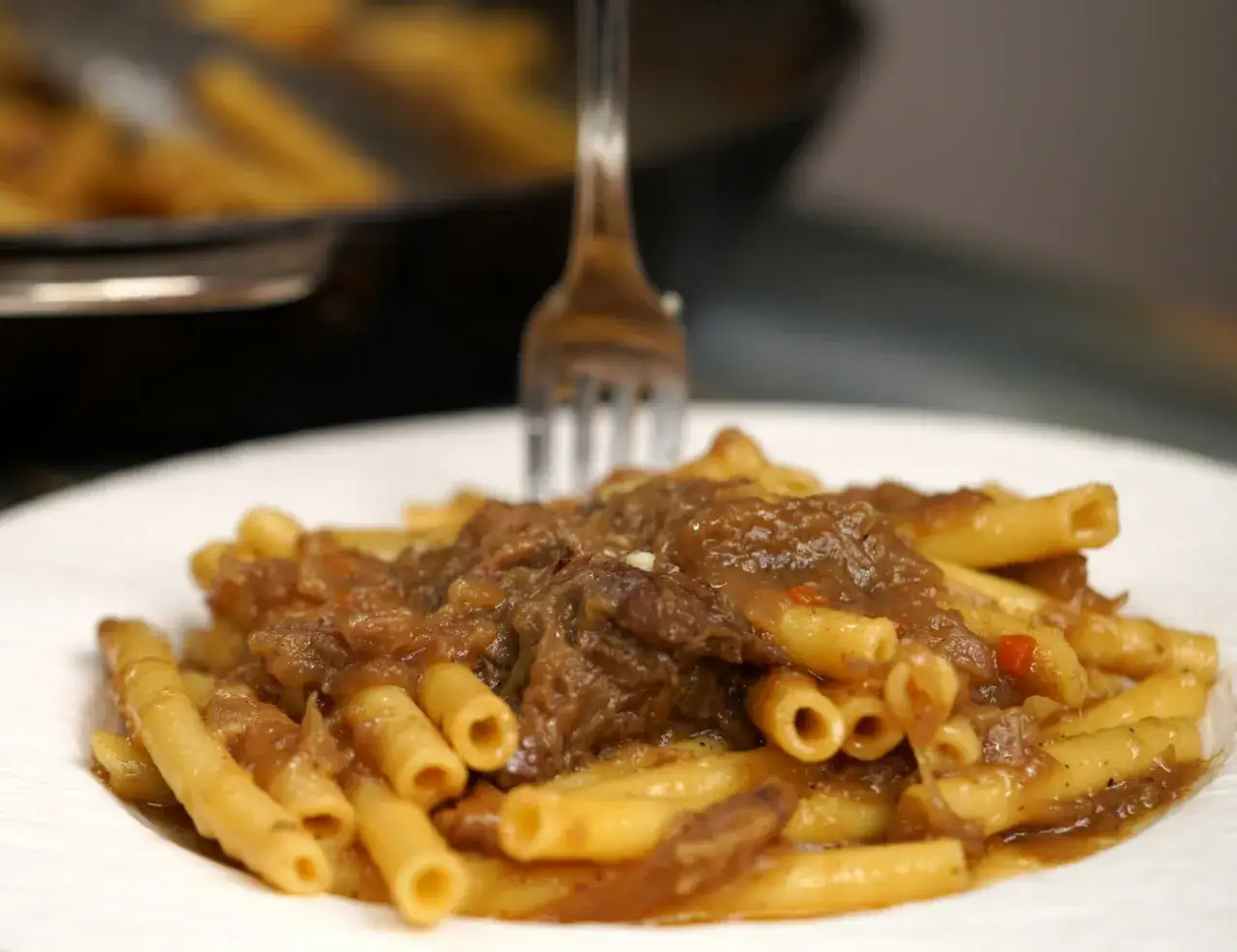 Piatto di ziti alla genovese fumanti, con la carne che si scioglie e un sugo ricco.