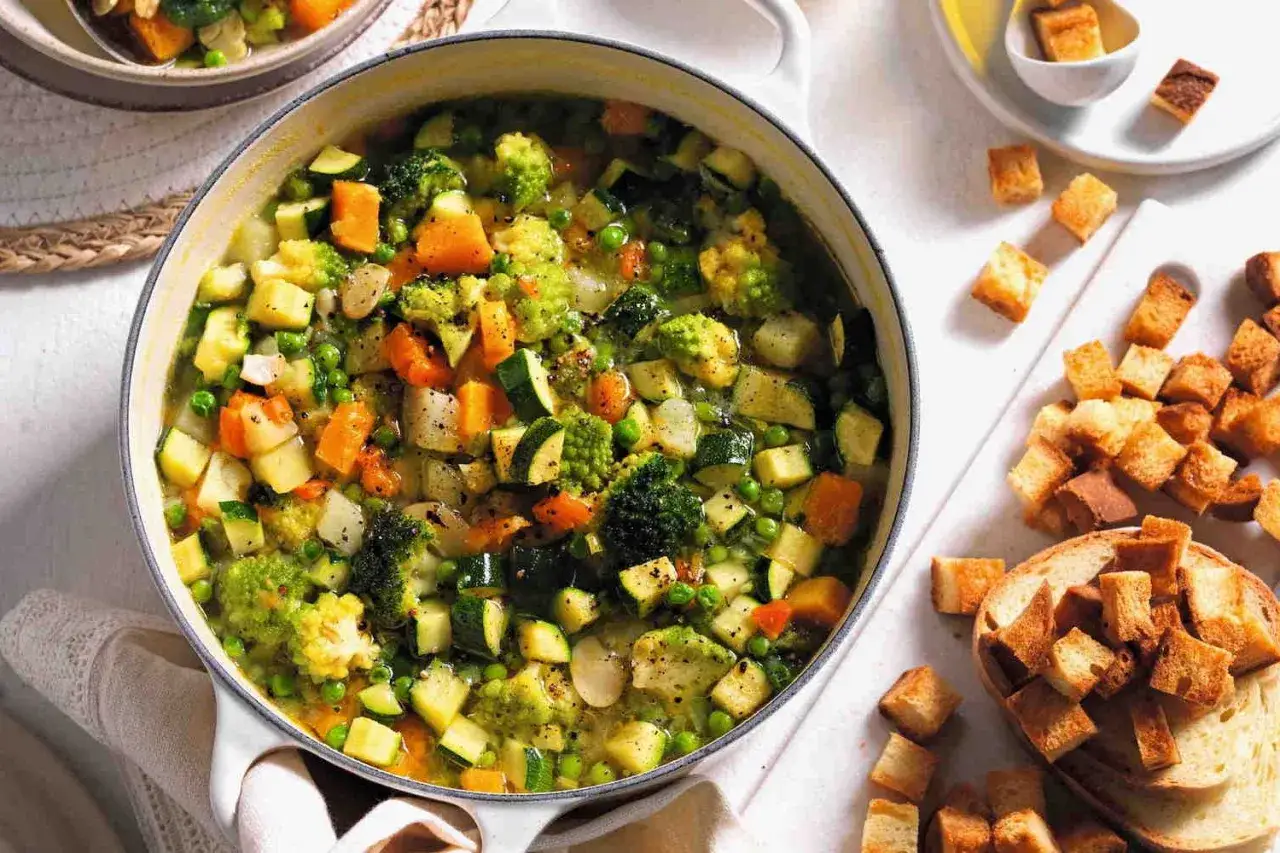 Un fumante minestrone di verdure, ricco di broccoli, carote, zucchine e piselli, pronto per essere gustato con crostini dorati.