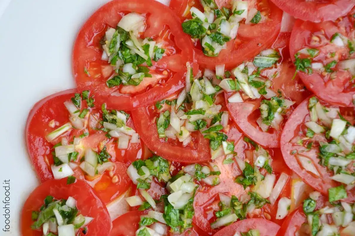 Fette di pomodoro fresco condite con cipolla tritata e erbe aromatiche. Un'insalata di pomodori semplice e gustosa.