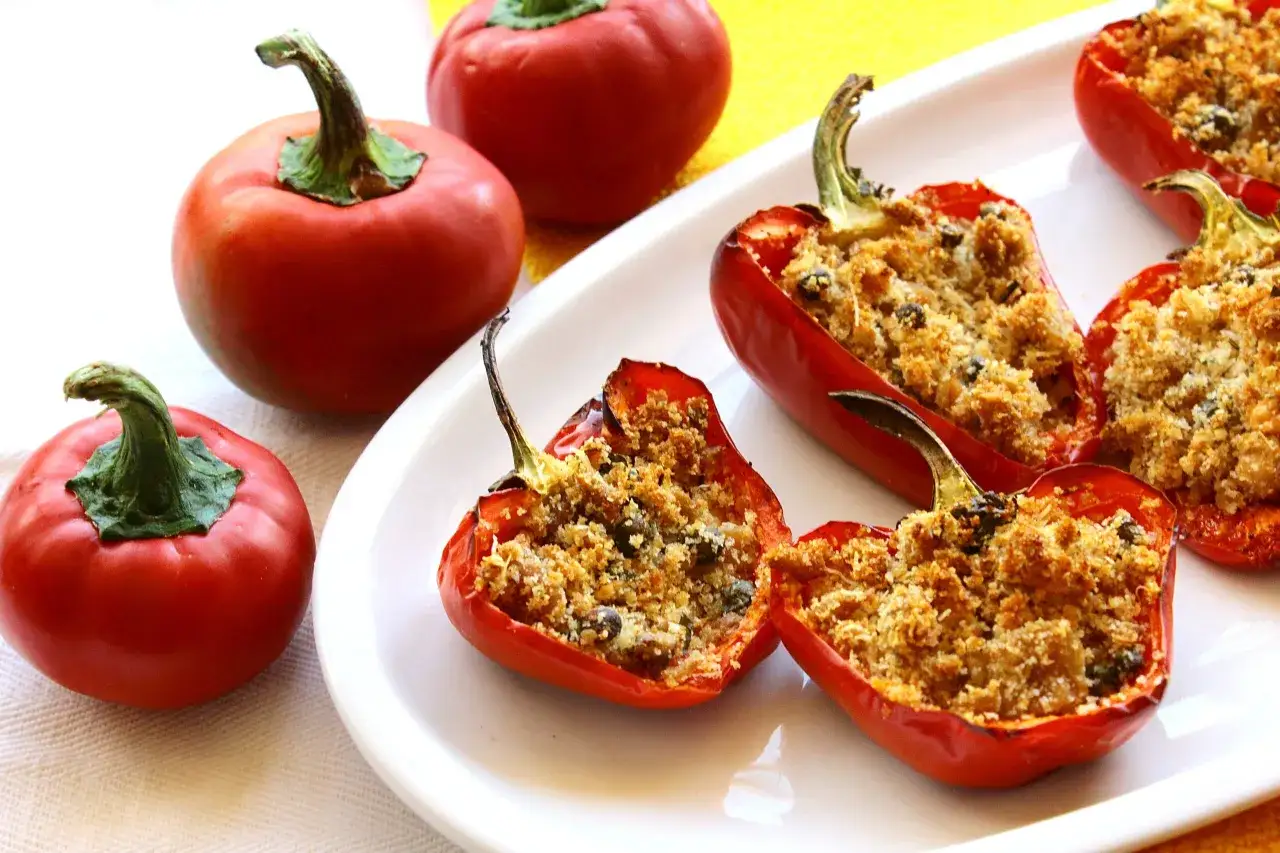Peperoni rossi ripieni di tonno e pangrattato, cotti al forno, su un piatto bianco.