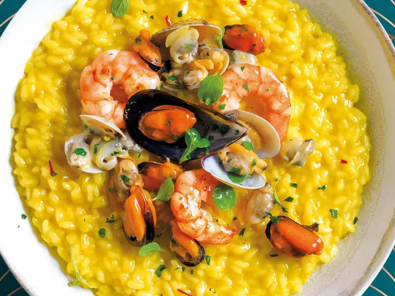 Risotto alla pescatora cremoso e dorato, ricco di gamberi, cozze e vongole fresche, guarnito con erbe aromatiche.
