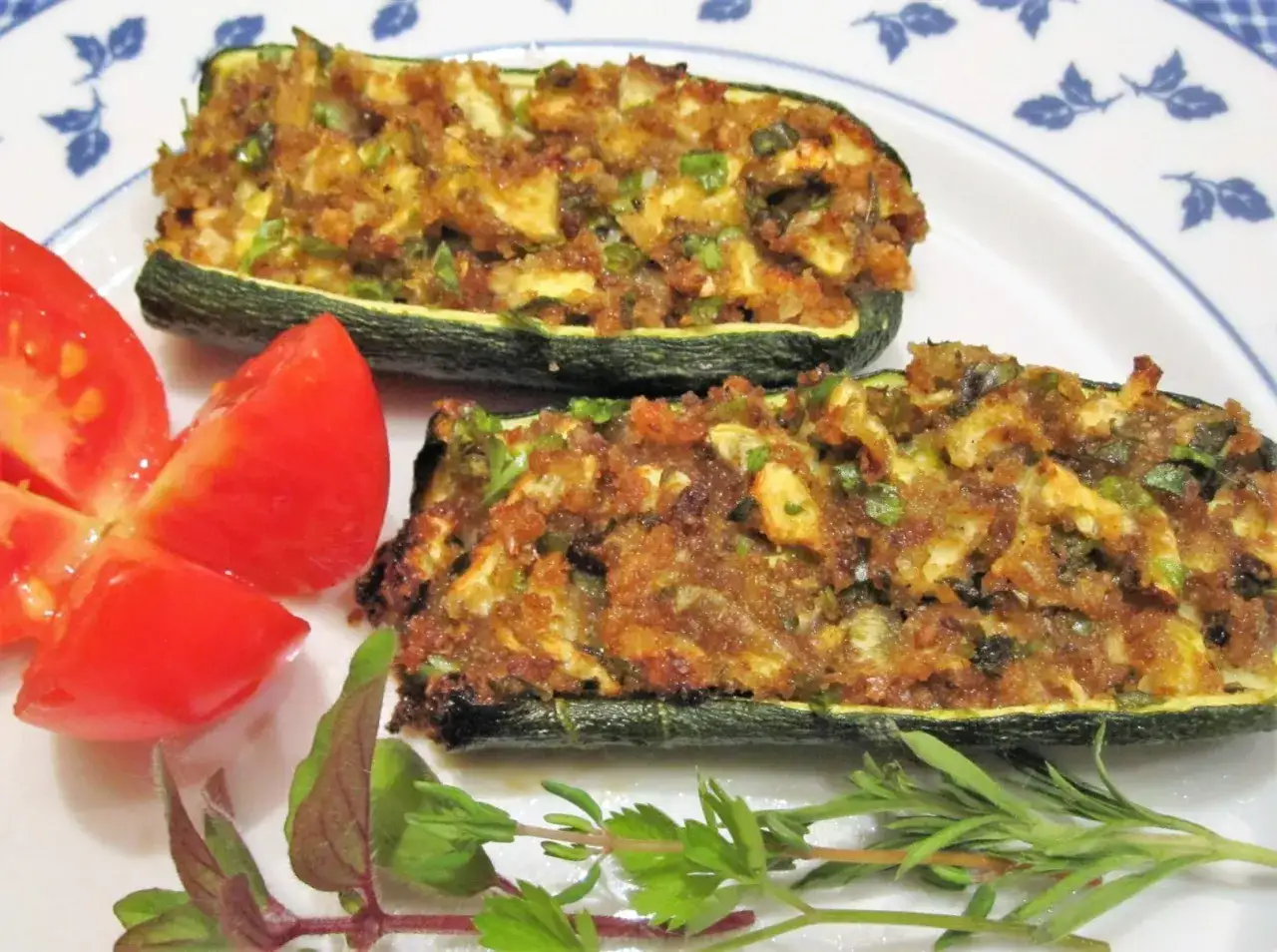 Zucchine al forno ripiene, dorate e profumate, servite con pomodoro fresco e erbe aromatiche.