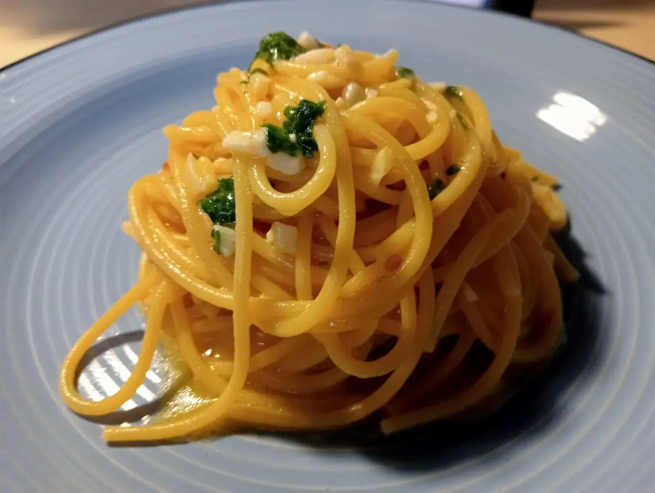Un piatto di pasta alla carrettiera, spaghetti conditi con aglio, olio, peperoncino e prezzemolo fresco, serviti su un piatto azzurro.