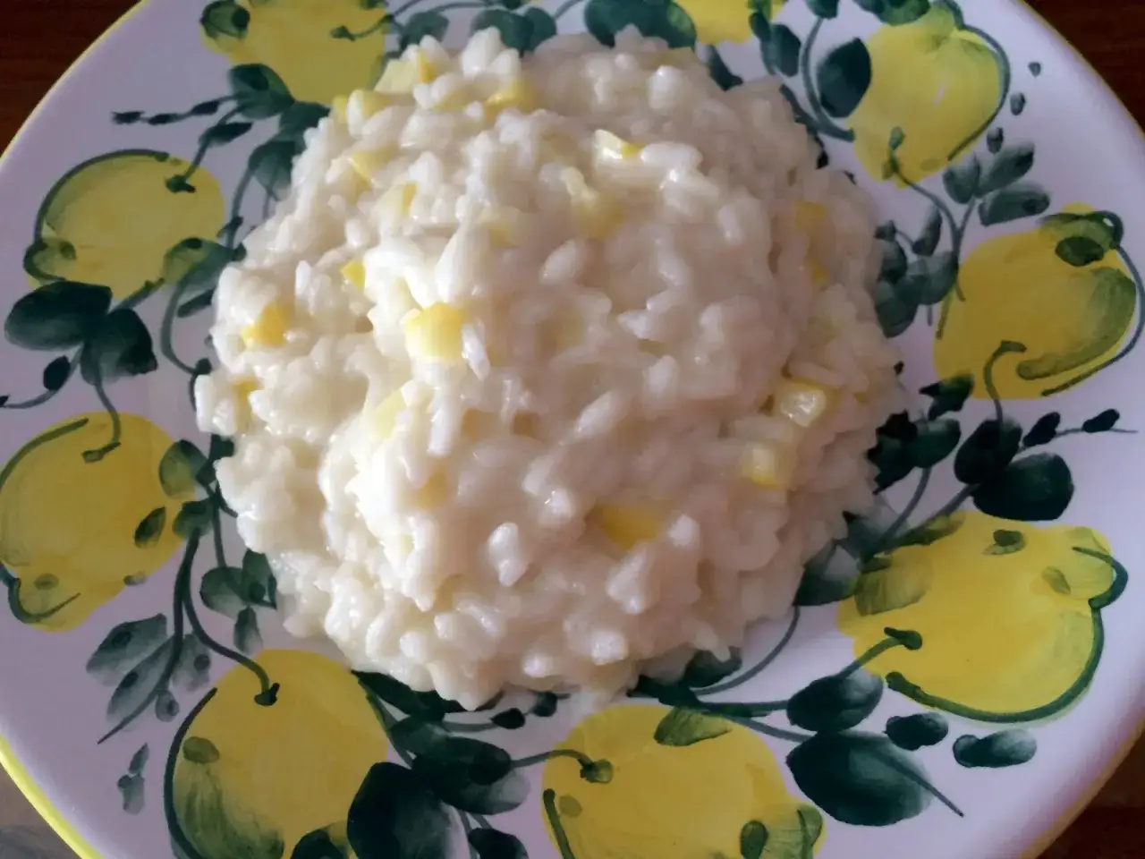Un cremoso risotto al limone, servito su un piatto decorato con limoni dipinti.