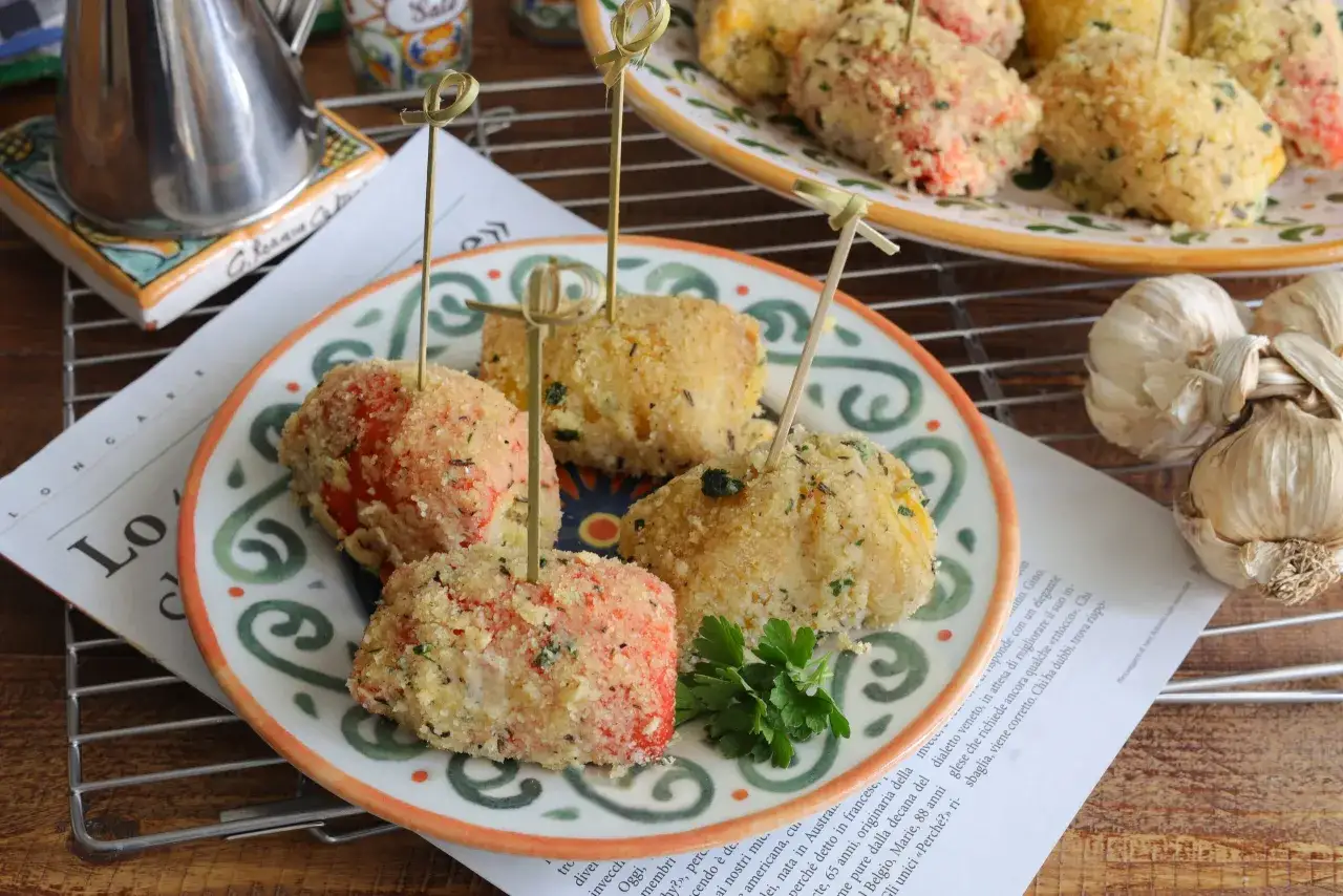 Peperoni ammollicati siciliani su un piatto decorato, con stuzzicadenti. Accanto, aglio e una brocca.