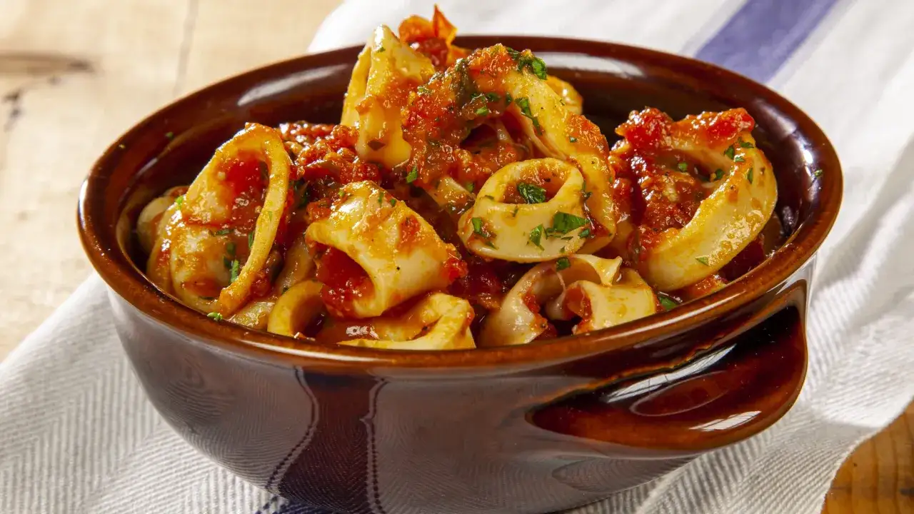 Calamari in umido, succulenti anelli di calamaro cotti in un ricco sugo di pomodoro e erbe aromatiche, serviti in una ciotola di terracotta.