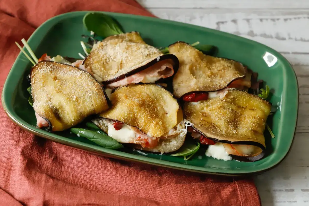 Involtini di melanzane gratinati con prosciutto e formaggio, serviti su un letto di insalata verde.