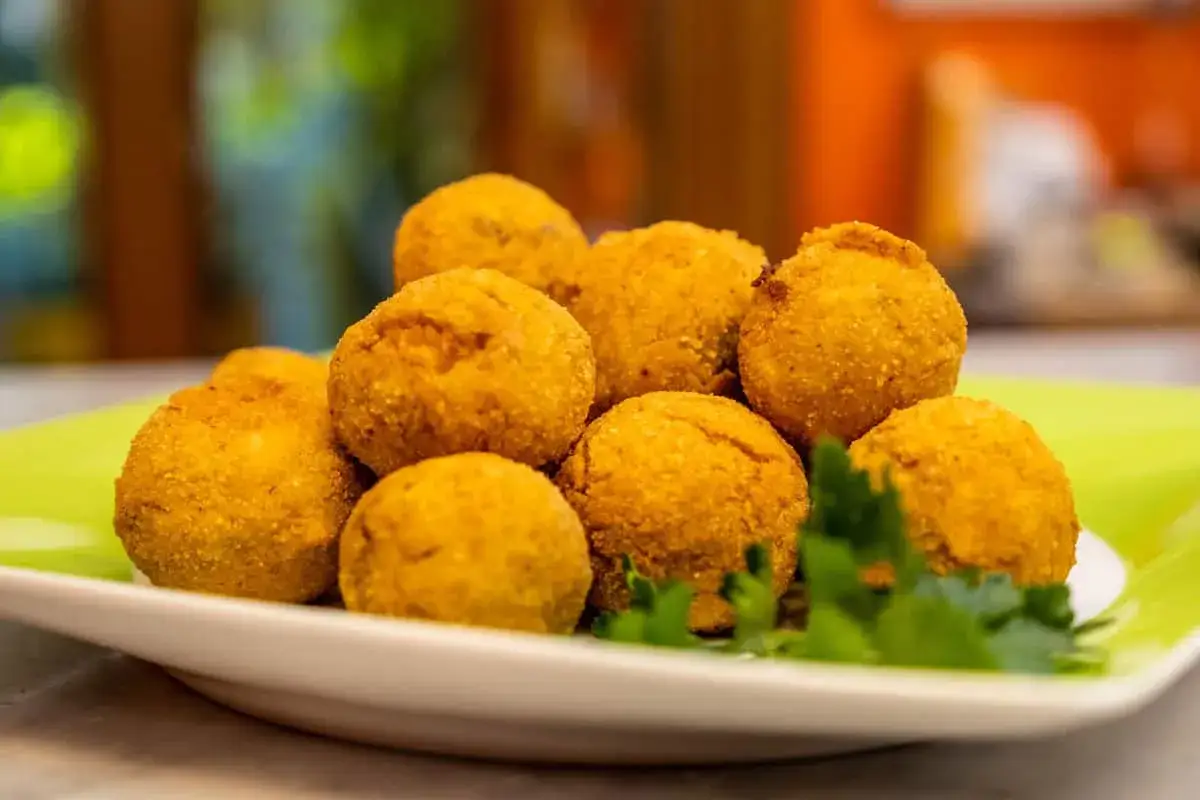 Un mucchio di dorate polpette di pesce, croccanti fuori e morbide dentro, servite su un piatto verde con prezzemolo fresco.