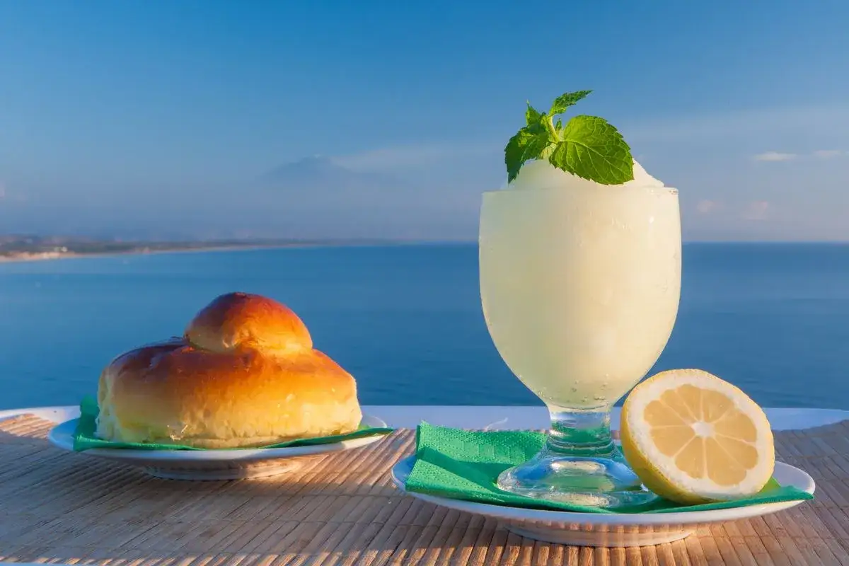 Granita al limone fatta in casa, con brioche e limone fresco, sullo sfondo del mare e dell'Etna.