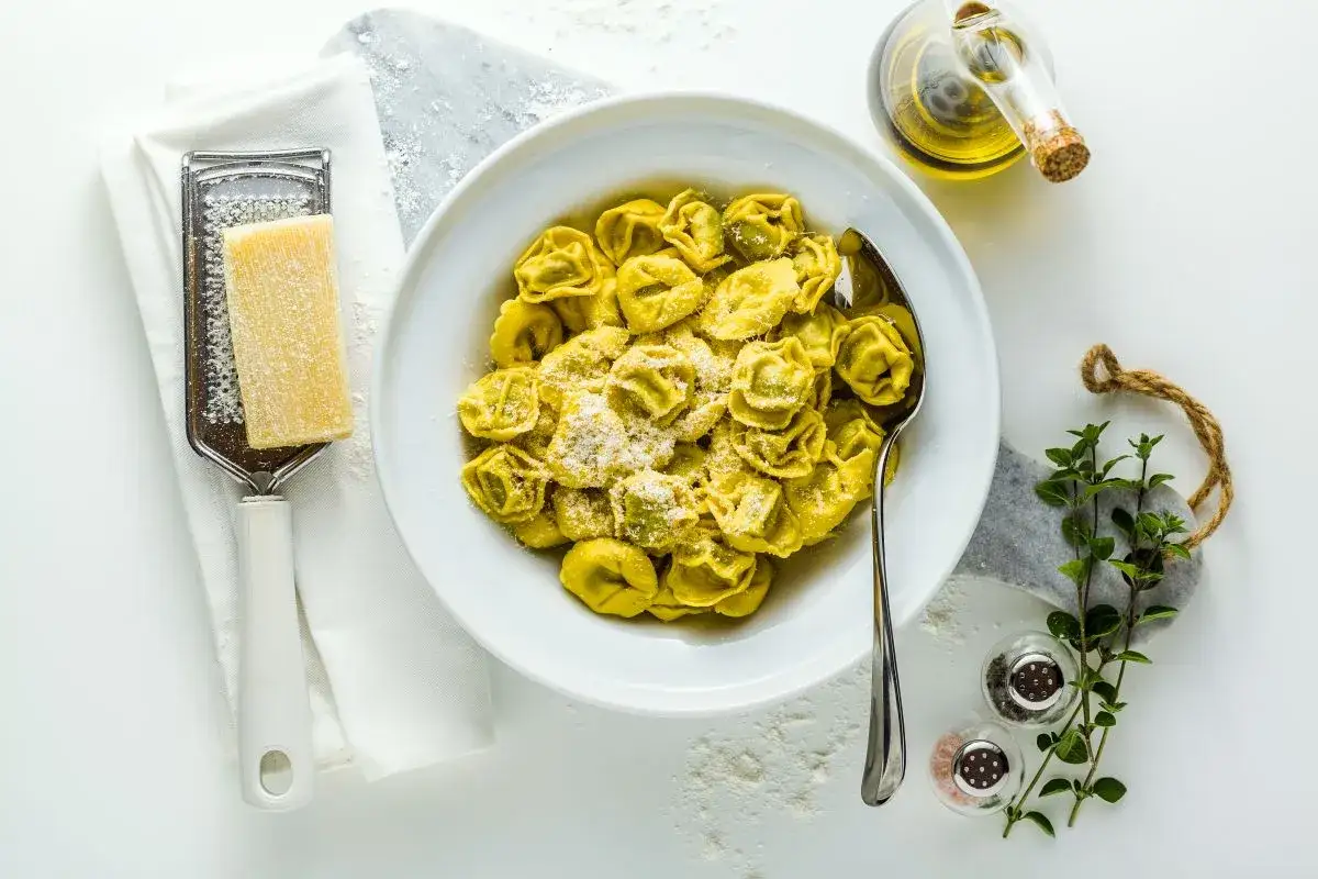Tortellini burro e salvia in una ciotola bianca, con parmigiano grattugiato, olio d'oliva e erbe aromatiche.